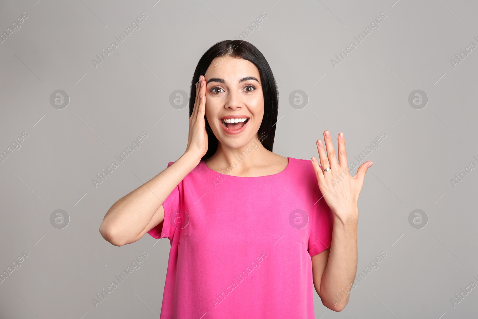 Photo of Emotional young woman wearing beautiful engagement ring on grey background