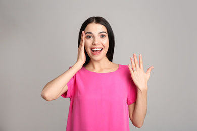 Photo of Emotional young woman wearing beautiful engagement ring on grey background