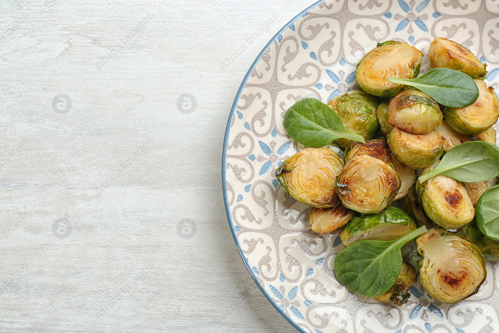 Photo of Delicious roasted brussels sprouts with basil on white wooden table, top view. Space for text