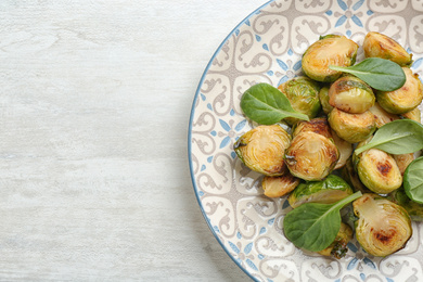 Photo of Delicious roasted brussels sprouts with basil on white wooden table, top view. Space for text