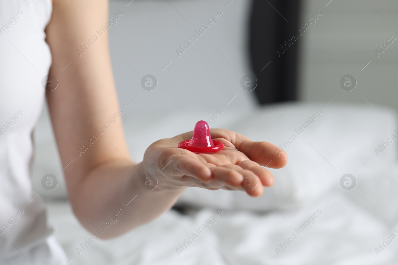 Photo of Woman holding unpacked condom in bedroom, closeup. Safe sex