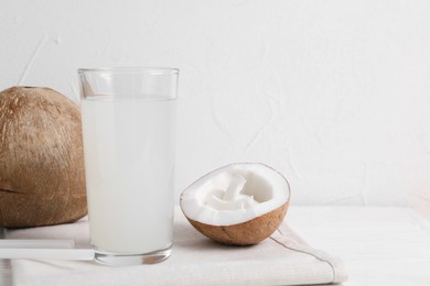 Photo of Glass of coconut water and nuts on white table. Space for text