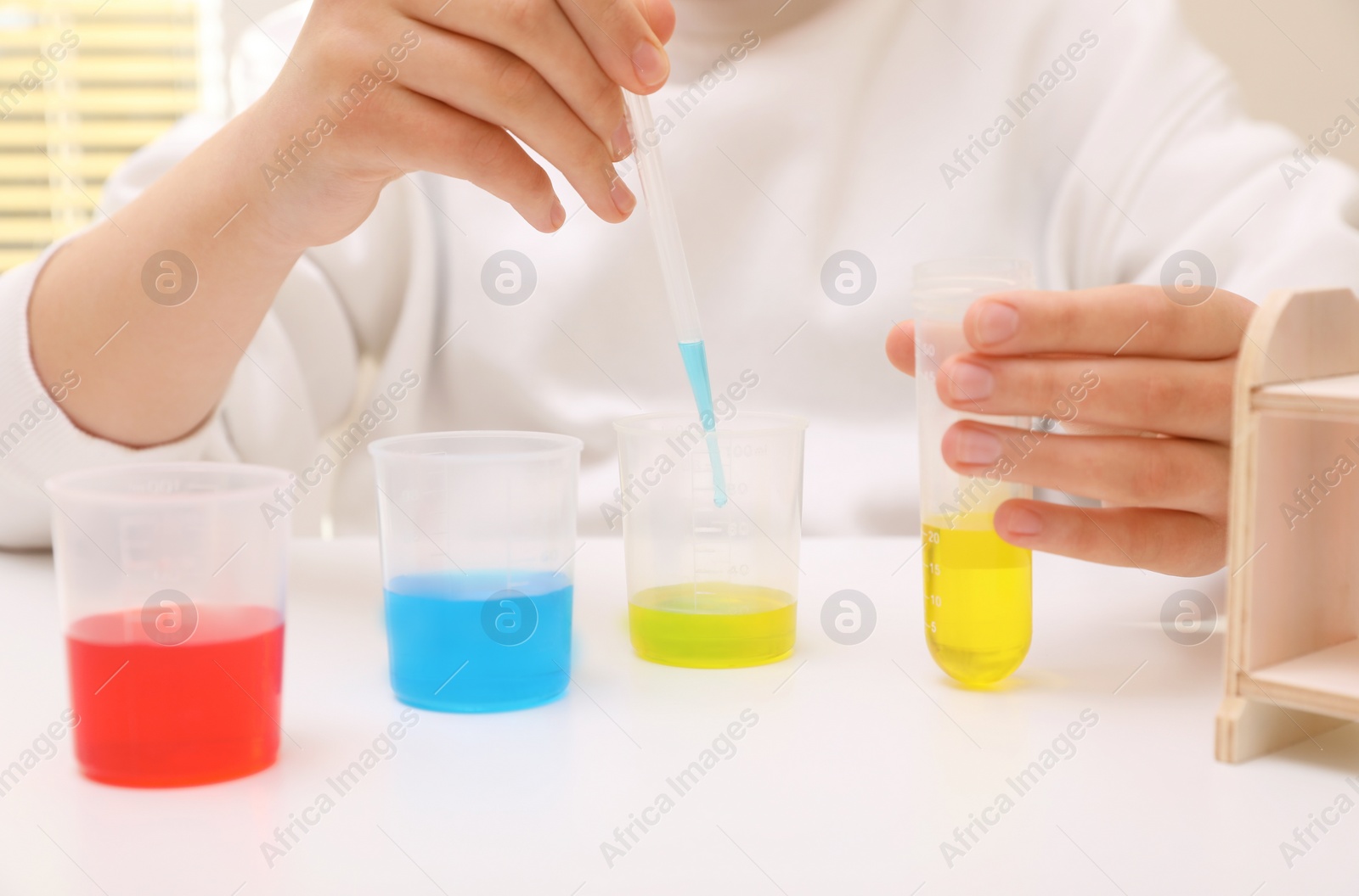 Photo of Girl mixing colorful liquids at white table indoors, closeup. Chemical experiment set for kids