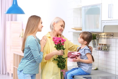Photo of Beautiful mature lady, daughter and grandchild with gifts in kitchen. Happy Women's Day