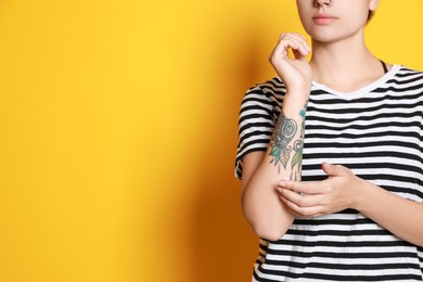 Photo of Woman applying cream on her arm with tattoos against yellow background, closeup. Space for text