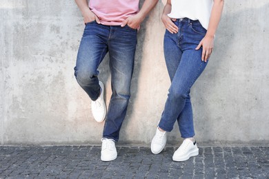 Photo of People in stylish jeans near grey wall outdoors, closeup