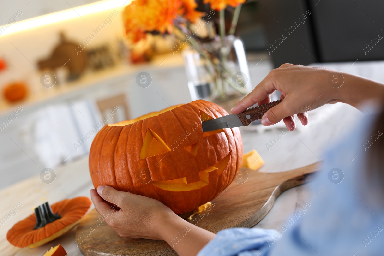 Photo of Woman making pumpkin jack o'lantern at table in kitchen, closeup. Halloween celebration