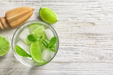 Refreshing beverage with mint and lime in glass on wooden background, top view