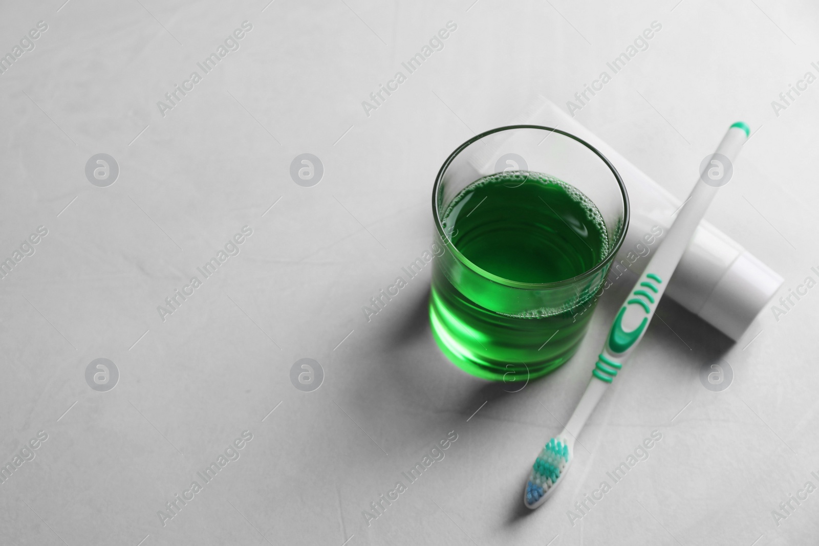 Photo of Fresh mouthwash in glass, toothpaste and toothbrush on light background. Space for text