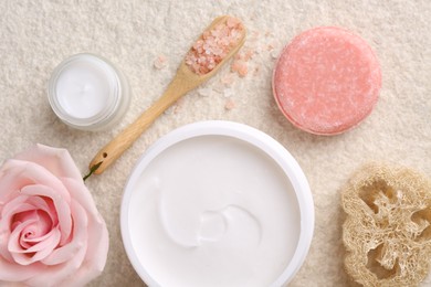 Flat lay composition with moisturizing cream in open jar and other body care products on light textured table