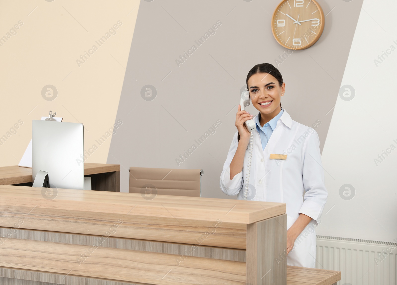 Photo of Receptionist talking on telephone at desk in modern clinic