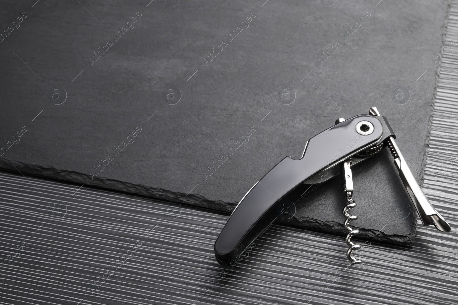 Photo of One corkscrew (sommelier knife) on black wooden table, above view. Space for text