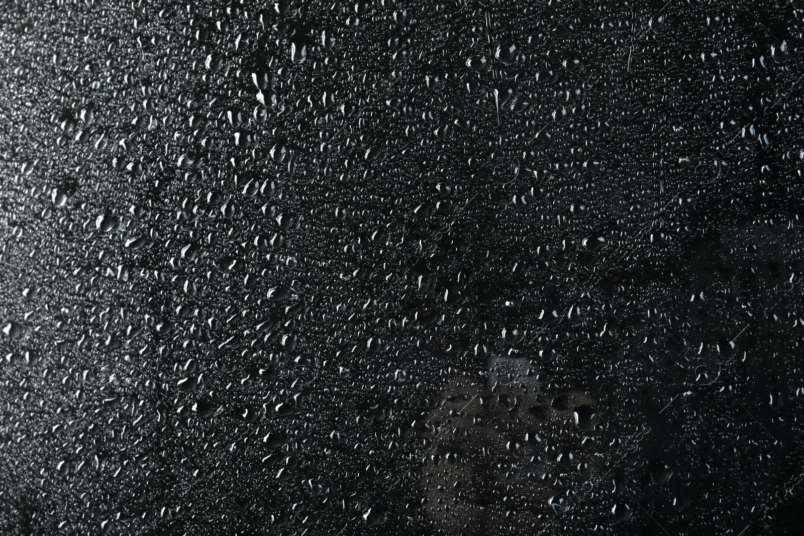 Photo of Glass with rain drops against dark background