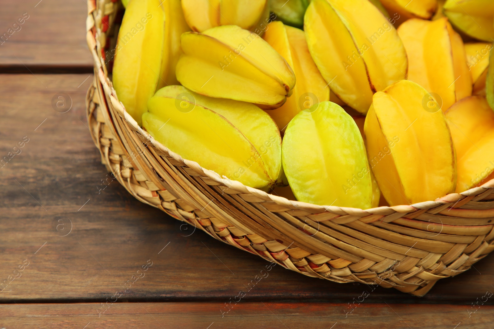 Photo of Delicious ripe carambolas in wicker basket on wooden table, closeup