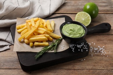 Photo of Serving board with french fries, avocado dip, rosemary and lime served on wooden table