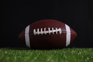 Photo of American football ball on green grass against black background