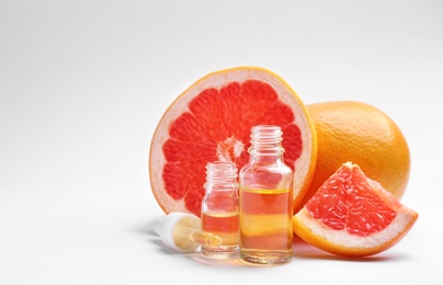 Bottles of essential oil and fresh grapefruits on white background