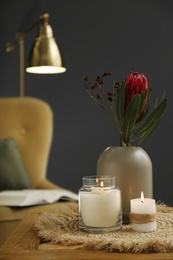 Vase with beautiful protea flowers and burning candles on wooden table indoors. Interior elements