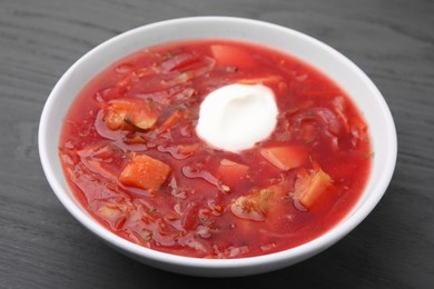 Photo of Tasty borscht with sour cream on grey wooden table, closeup