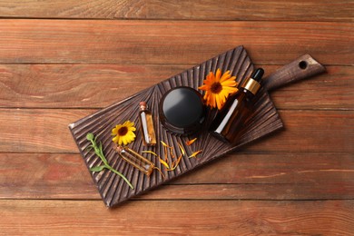 Bottles and jar of cosmetic products with beautiful calendula flowers on wooden table, top view