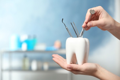 Dentist putting professional tool into tooth shaped holder in clinic, closeup. Space for text