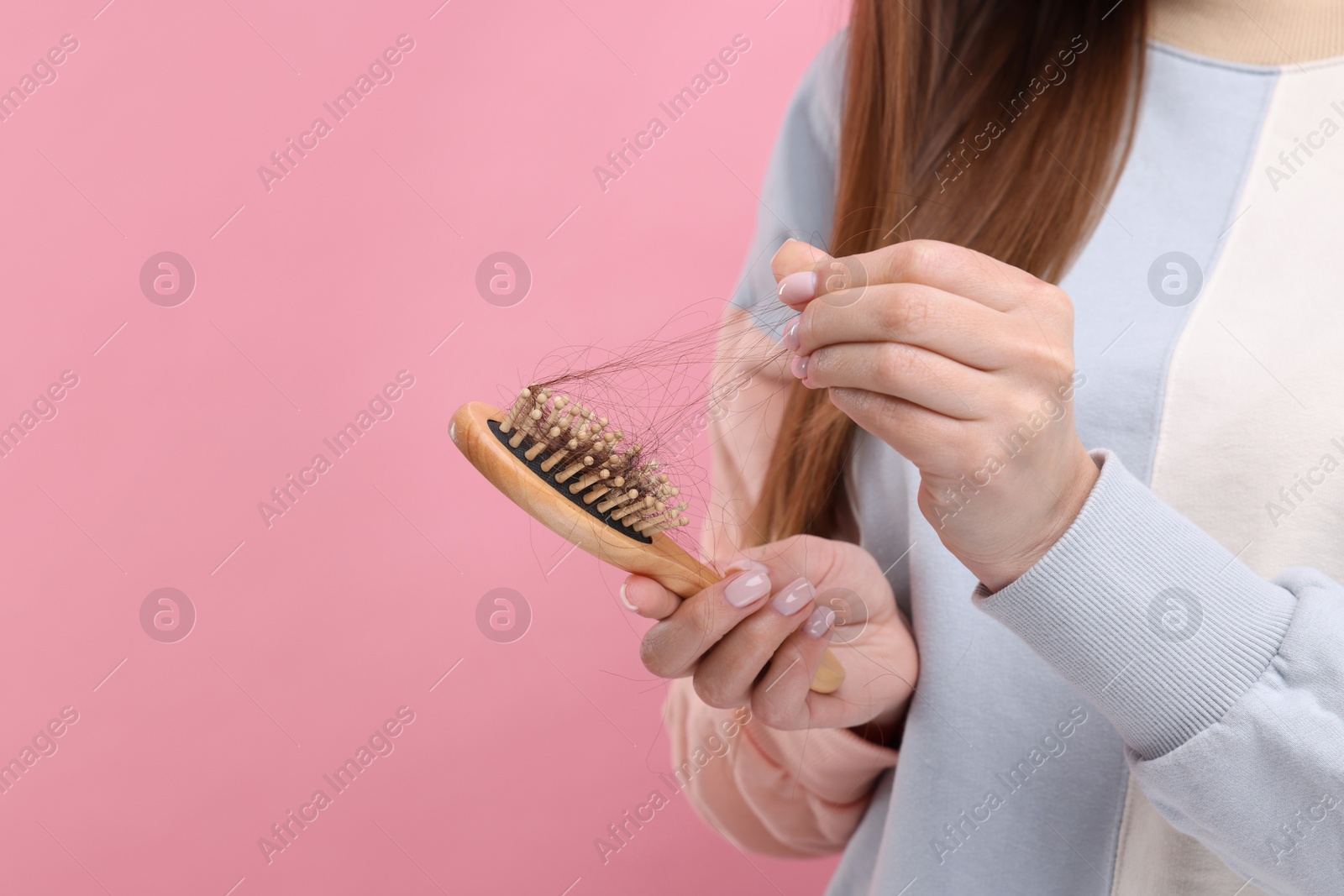 Photo of Woman untangling her lost hair from brush on pink background, closeup and space for text. Alopecia problem