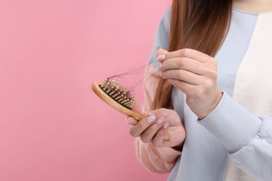 Woman untangling her lost hair from brush on pink background, closeup and space for text. Alopecia problem