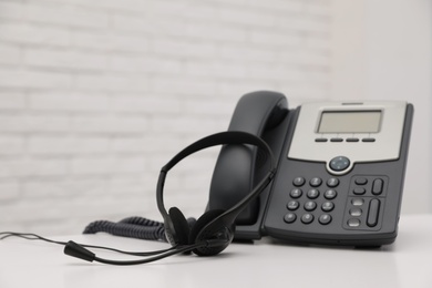 Photo of Desktop telephone and headset on white table in office, space for text. Hotline service