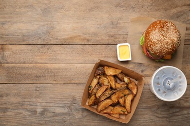 Flat lay composition with tasty burger and potato wedges on wooden table, space for text. Fast food