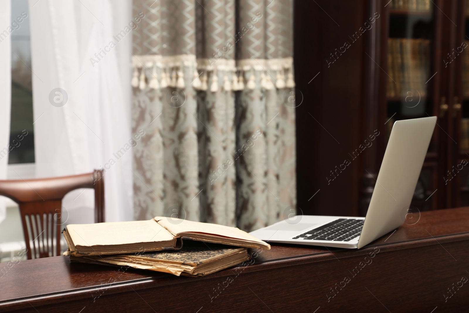 Photo of Old books and laptop on wooden table in library reading room