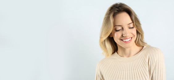 Portrait of happy young woman with beautiful blonde hair and charming smile on light background