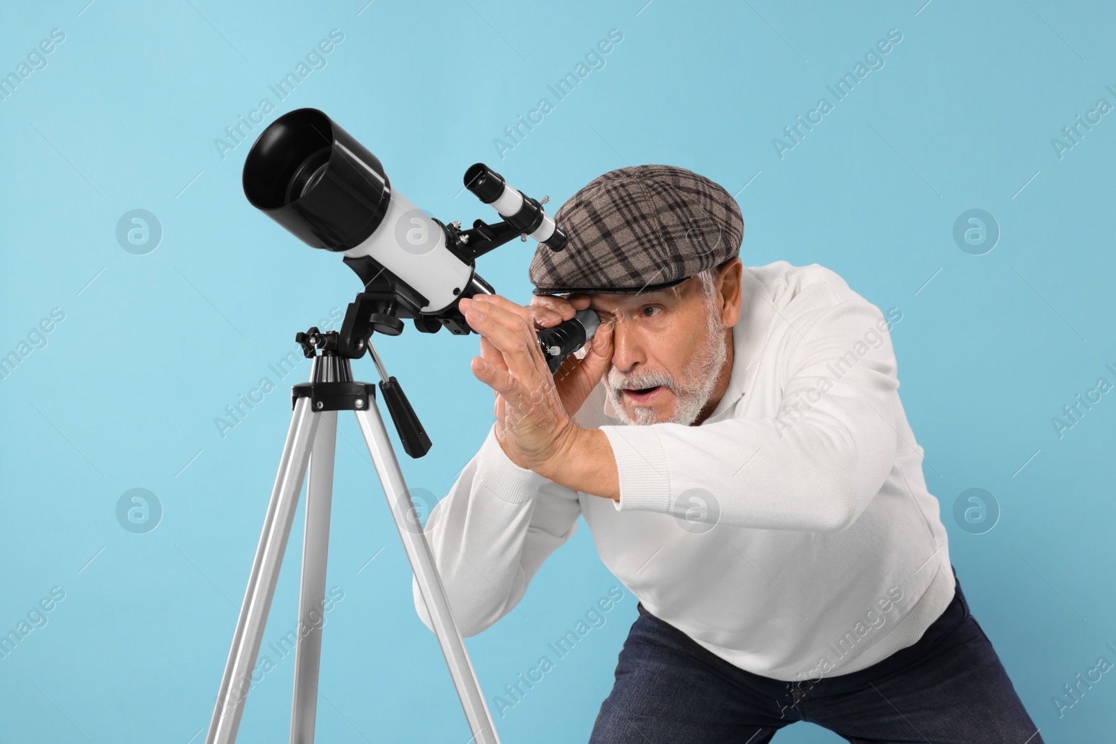 Photo of Senior astronomer looking at stars through telescope on light blue background