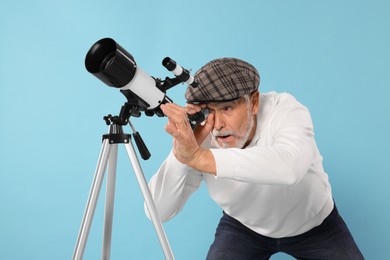 Senior astronomer looking at stars through telescope on light blue background