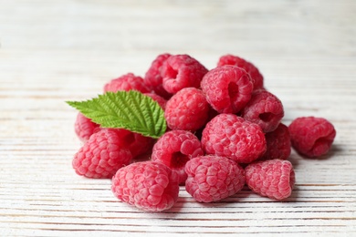 Photo of Delicious fresh ripe raspberries with leaves on white wooden table, closeup view