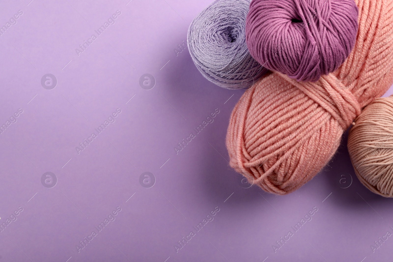 Photo of Soft woolen yarns on violet background, flat lay. Space for text