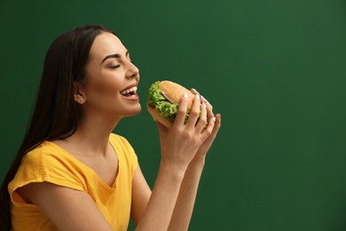 Young woman eating tasty burger on color background. Space for text