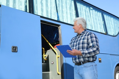 Professional driver with clipboard near bus. Passenger transportation