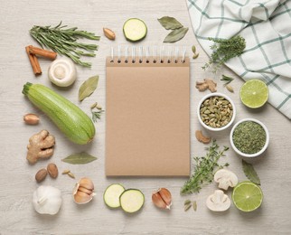 Open recipe book and different ingredients on white wooden table, flat lay. Space for text