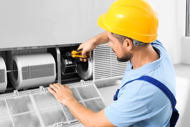 Professional male technician repairing air conditioner indoors