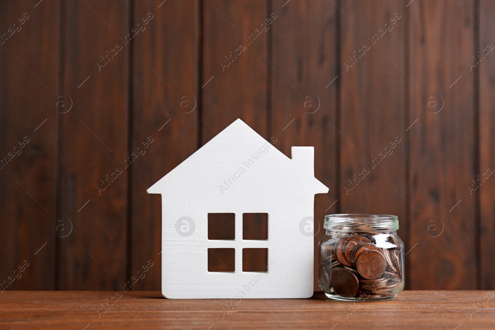 Photo of House model and jar with coins on table against wooden background. Space for text