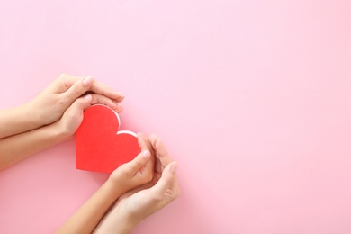 Woman and child holding red heart on color background, top view