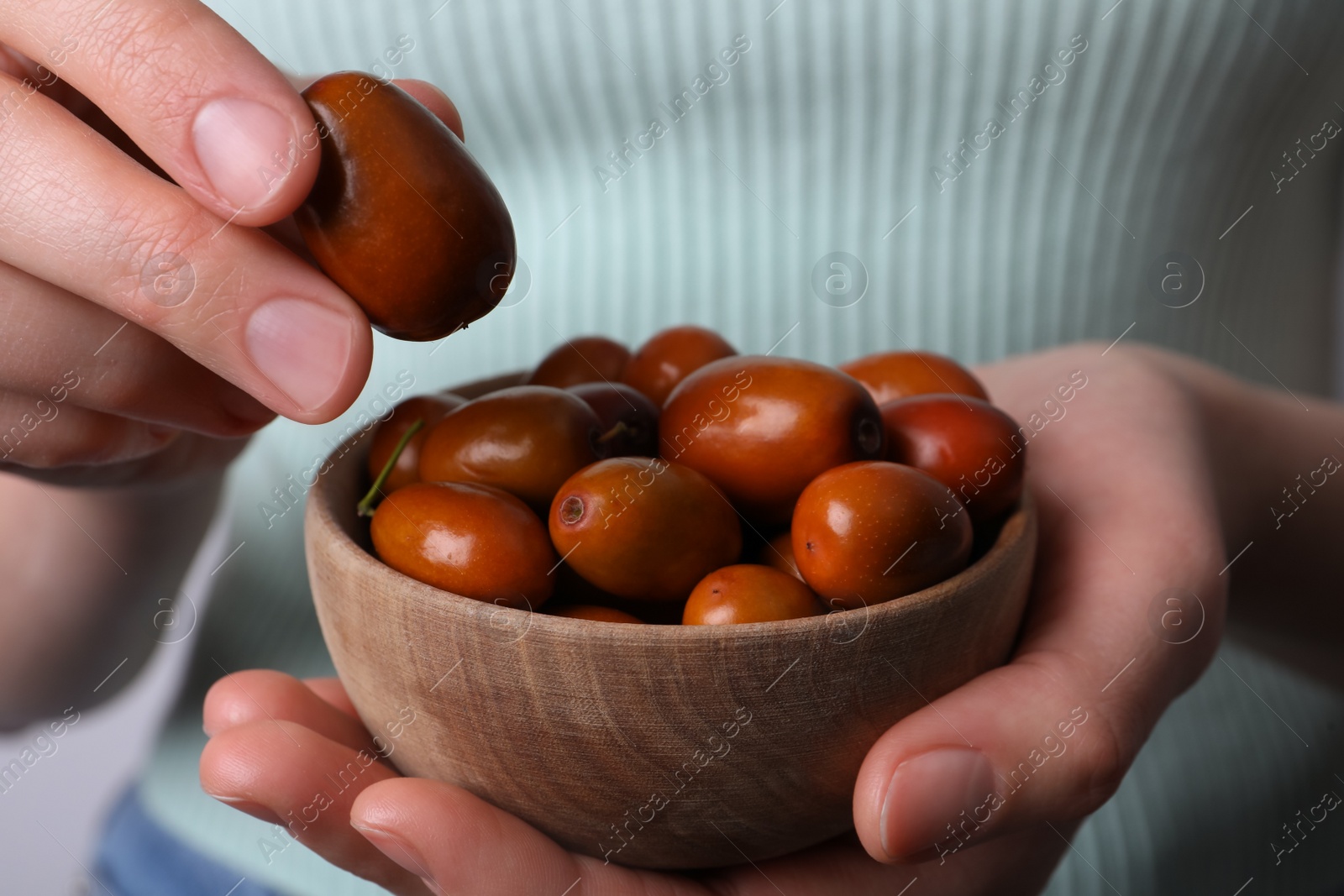 Photo of Woman holding wooden bowl with fresh Ziziphus jujuba fruits, closeup