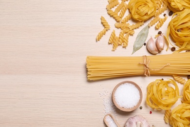 Flat lay composition with different types of pasta on light wooden table, space or text