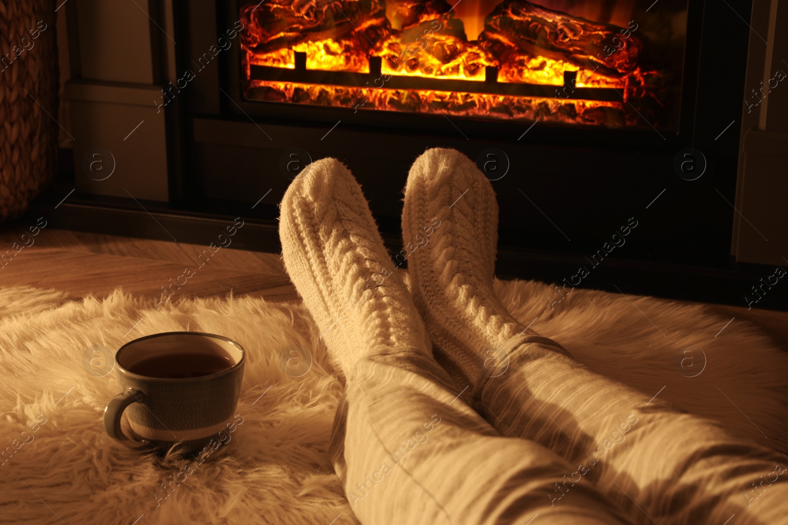 Photo of Woman in knitted socks resting near fireplace at home, closeup