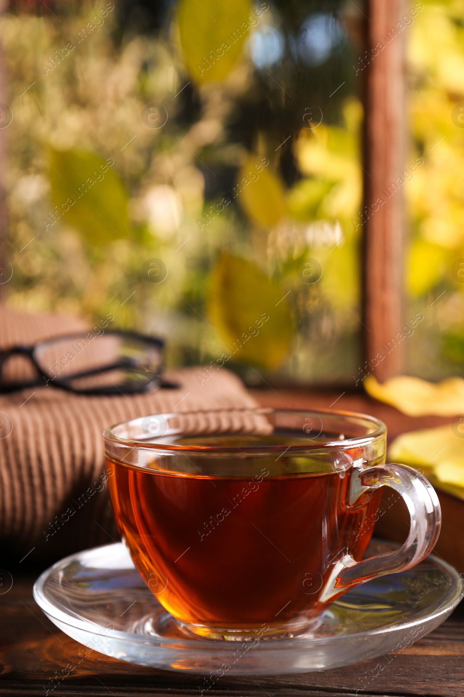 Photo of Cup of aromatic tea and soft sweater on wooden windowsill indoors, closeup. Autumn atmosphere
