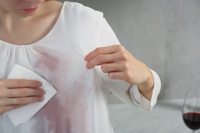 Woman wiping wine stain on her clothes indoors, closeup