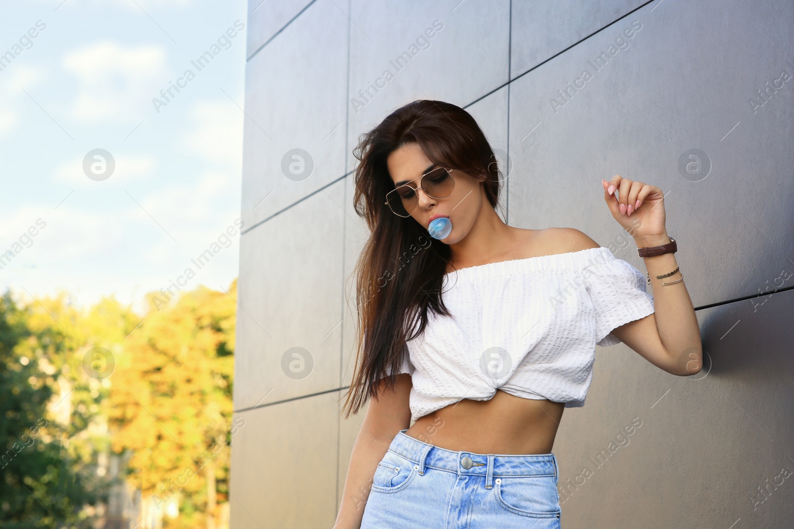 Photo of Beautiful woman blowing gum near dark tiled wall outdoors, space for text