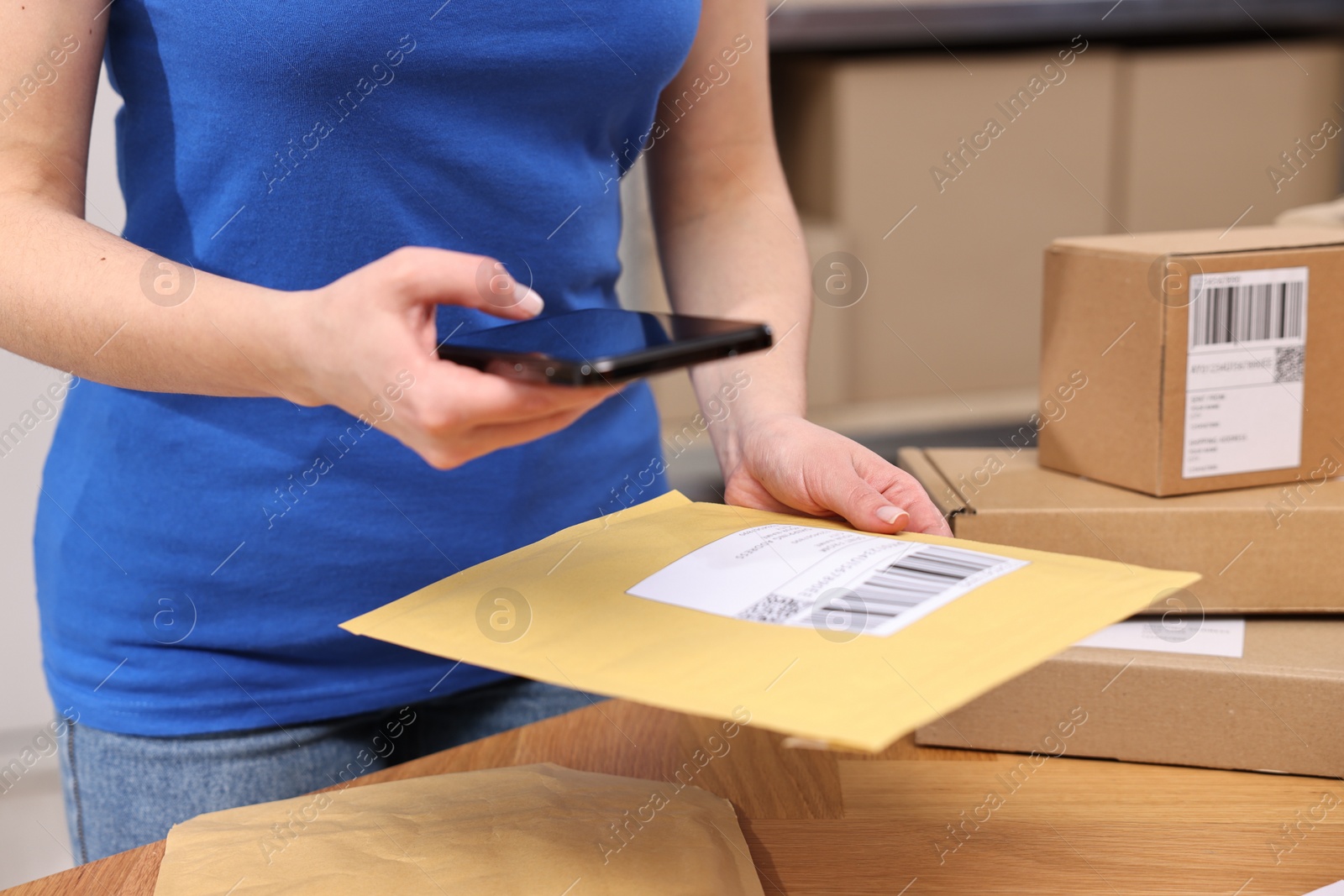 Photo of Parcel packing. Post office worker with smartphone reading barcode at wooden table indoors, closeup