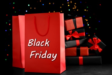 Photo of Paper shopping bags with gift boxes against blurred lights. Black Friday sale