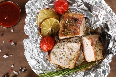 Photo of Pieces of delicious meat baked in foil with tomatoes and sauce on wooden table, flat lay